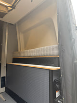 RV rental interior featuring a cushioned bench, lower textured cabinetry, and a fresh water inlet.