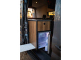 RV rental interior: a compact kitchen with wood cabinets, a lit fridge, and a pull-out table.