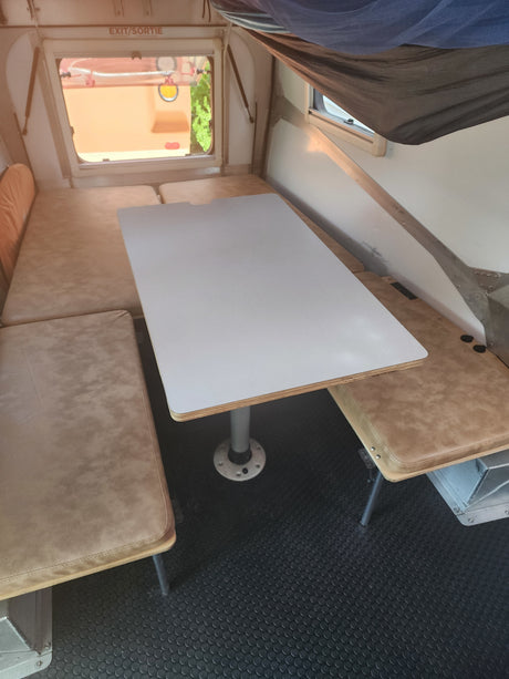 Cozy rv rental interior: central dining table, tan cushioned seating, and dark patterned floor. Ideal compact camper setup.