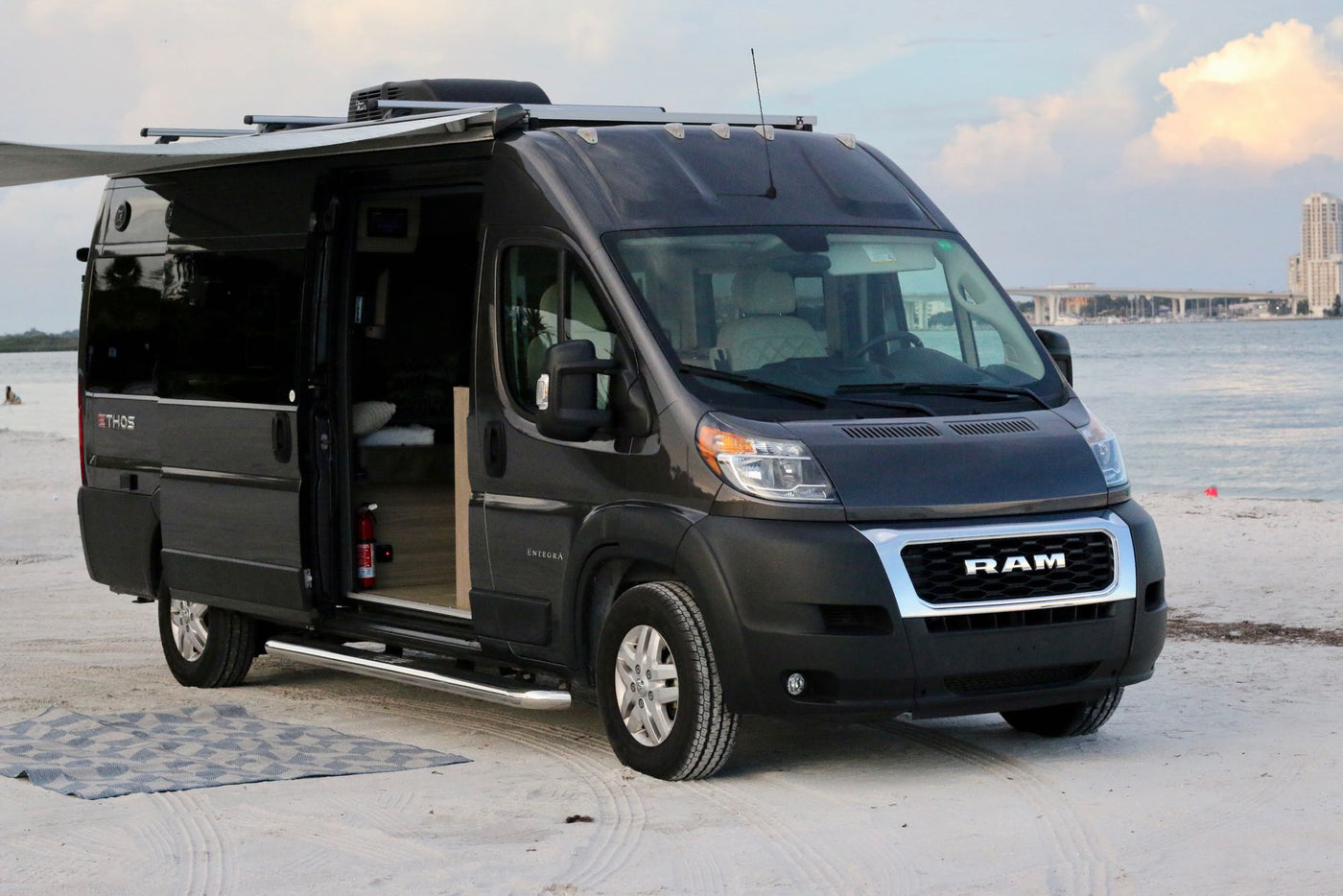  ready for adventure.|Coastal adventure awaits with this rv rental! A gray camper van with an awning and rug is parked on a sandy beach.||Explore this RV rental's compact kitchenette: sink — photo 8