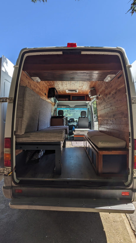 Inside a custom-built RV rental camper van, showing the cozy wooden interior, seating, and a cooler.