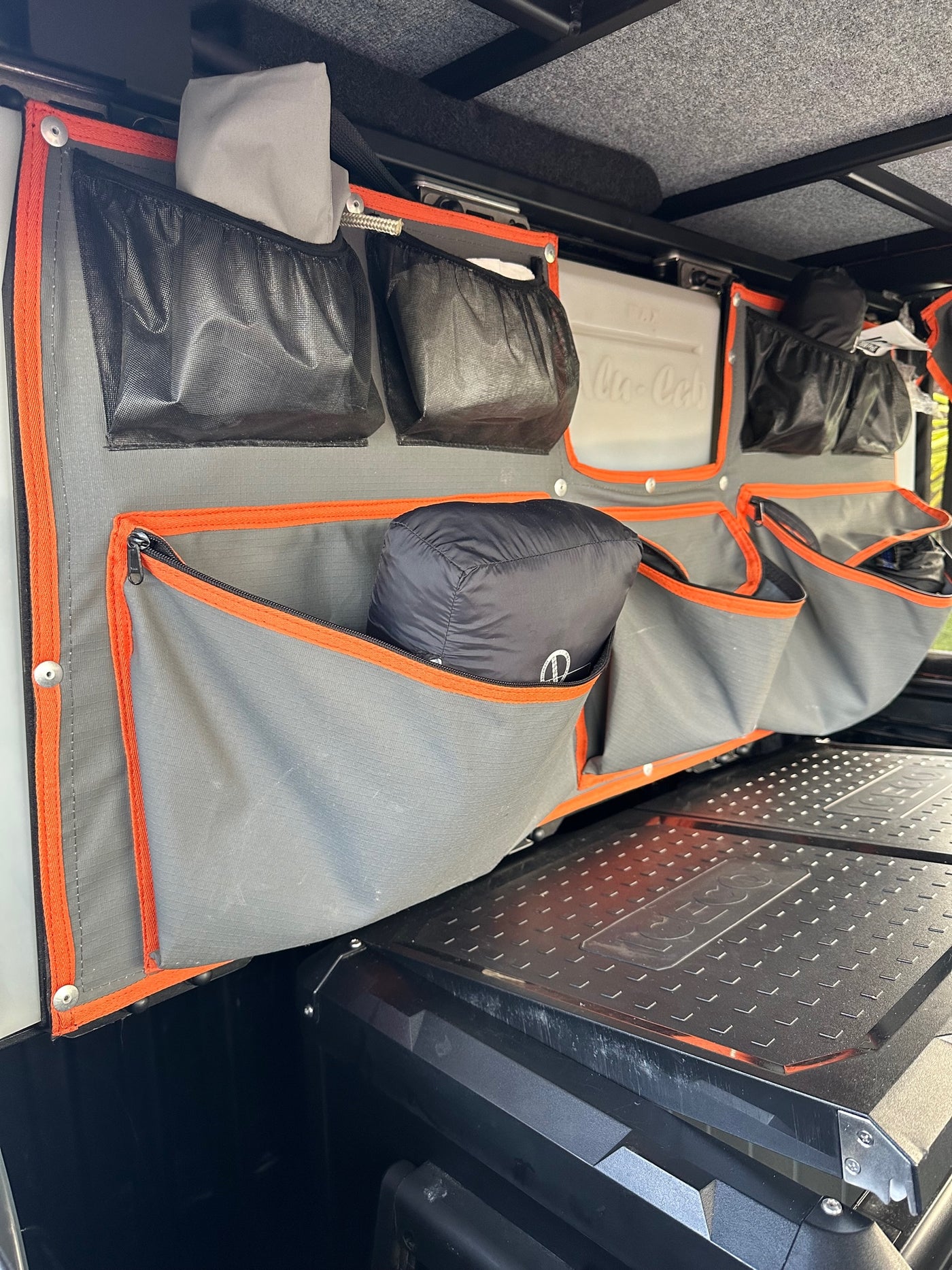 Organized RV rental interior: A multi-pocket grey fabric system over a cooler for travel gear. — photo 17