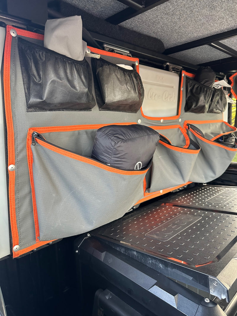 Organized RV rental interior: A multi-pocket grey fabric system over a cooler for travel gear. — photo 17