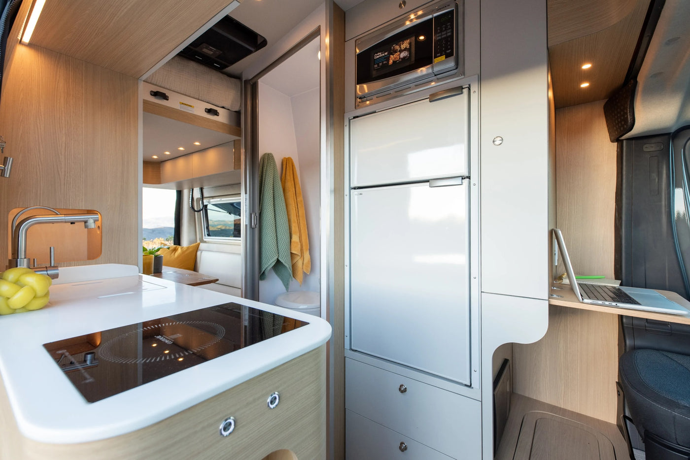 Inside a versatile rv rental: compact kitchen with induction cooktop, fridge, microwave, and cozy dining/workspace. — photo 5