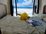 An RV rental offers a cozy bed view of the Bonneville Salt Flats, mountains, and sky. A Pikachu plush rests on the bed.