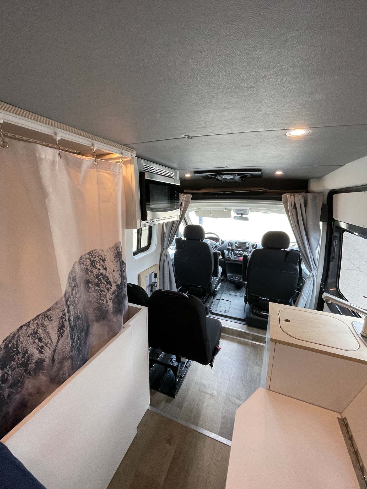 Interior of a modern RV rental, featuring a driver's cabin, swiveling seats, a compact kitchenette, and a unique mountain shower. — photo 9