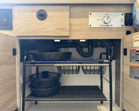 Inside an rv rental: kitchen cabinet with eco-HOT water heater panel, sink plumbing, and organized pot/pan storage.