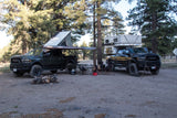 Custom Ram trucks with a rooftop tent & truck camper at a forest campsite. Explore the outdoors with an RV rental.
