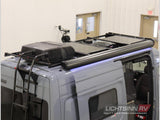 A modern gray camper van for RV rental, featuring rooftop AC, solar panels, ladder, and a blue-lit awning.