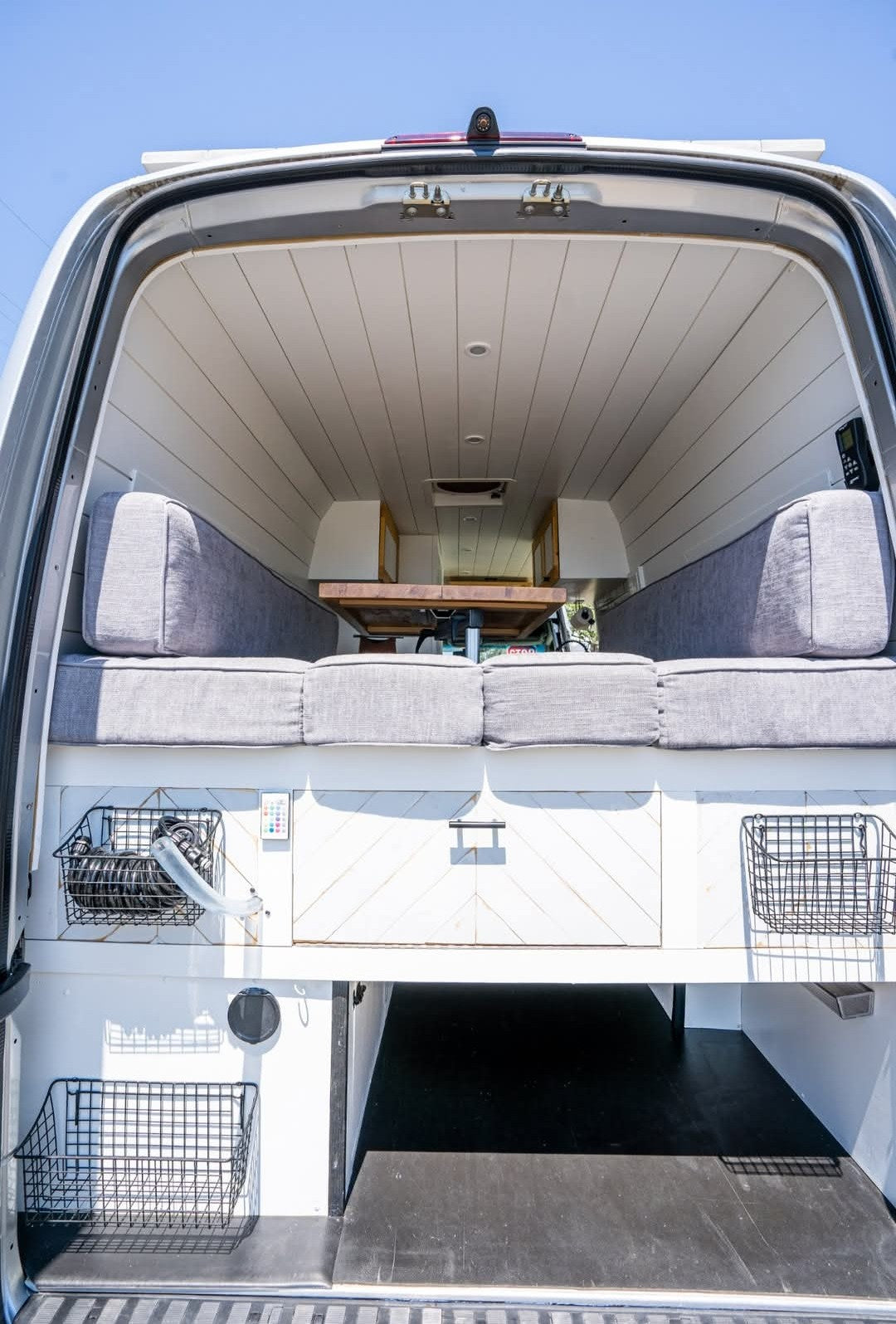 View from the back: This RV rental's camper van interior features a convertible gray bed/seating, table, and storage. — photo 18