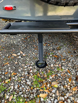 A travel trailer's rear light, utility line, and stabilizer jack on gravel ground for your RV rental.