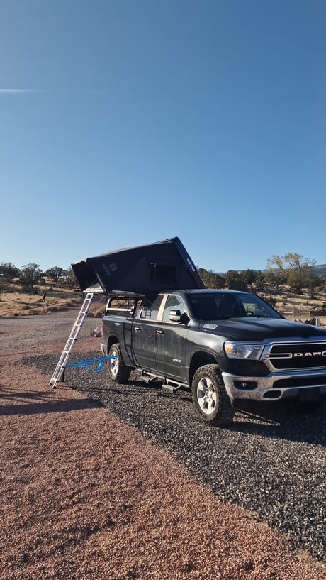 Black Ram pickup truck with iKamper rooftop tent and ladder on gravel. Perfect setup for an rv rental camping trip.