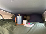 Cozy RV rental bed with a French press, mug, and a book on a wooden tray. Perfect for a relaxing morning in your camper.