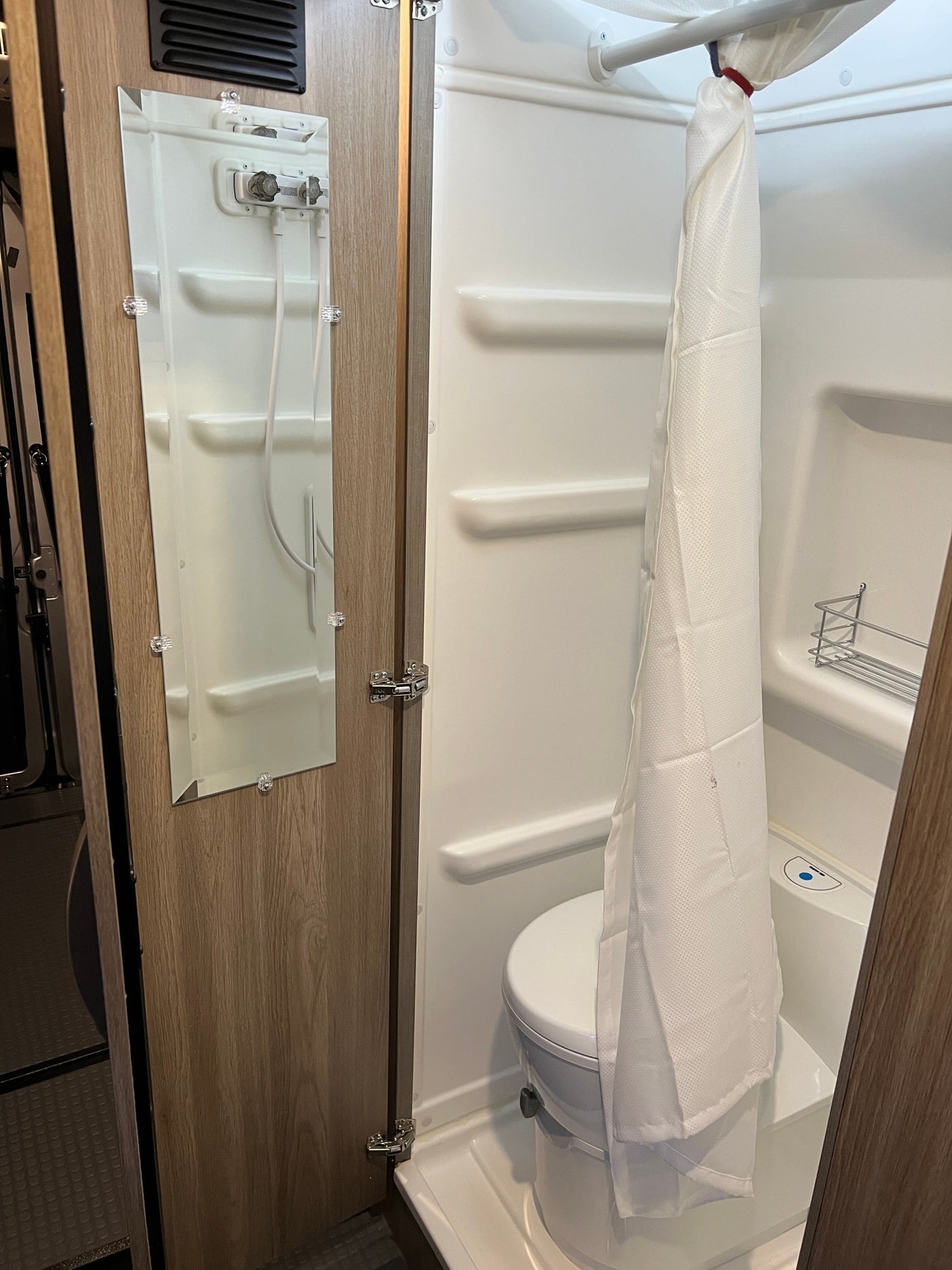 Inside an RV rental, discover a compact wet bath: toilet, shower stall with curtain, and a mirror on the door. — photo 7
