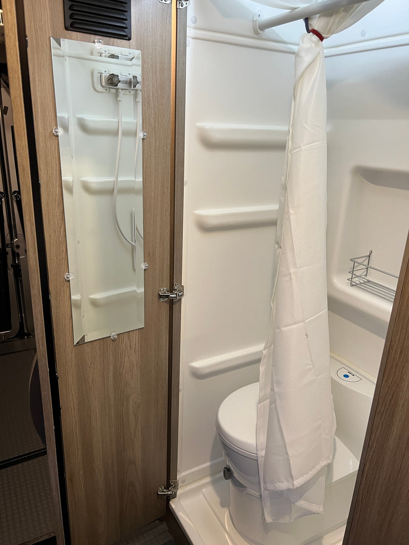 Inside an RV rental, discover a compact wet bath: toilet, shower stall with curtain, and a mirror on the door. — photo 7