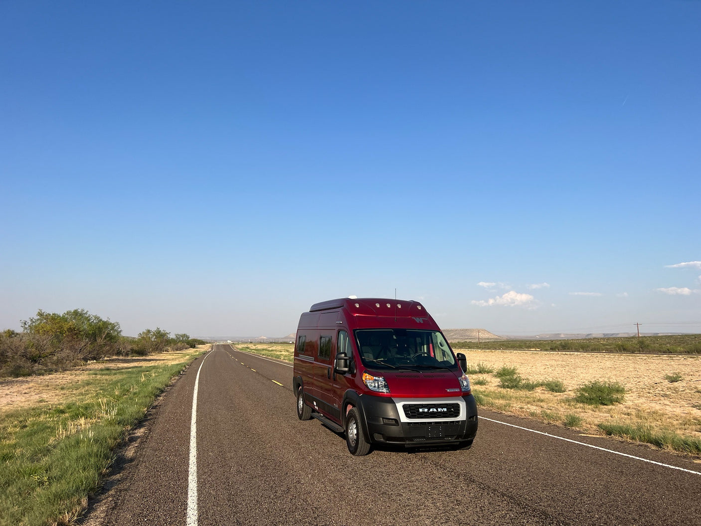 Red RV rental on an open road stretching into the distance under clear blue sky. Ideal for a scenic road trip adventure.