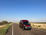 Red RV rental on an open road stretching into the distance under clear blue sky. Ideal for a scenic road trip adventure.