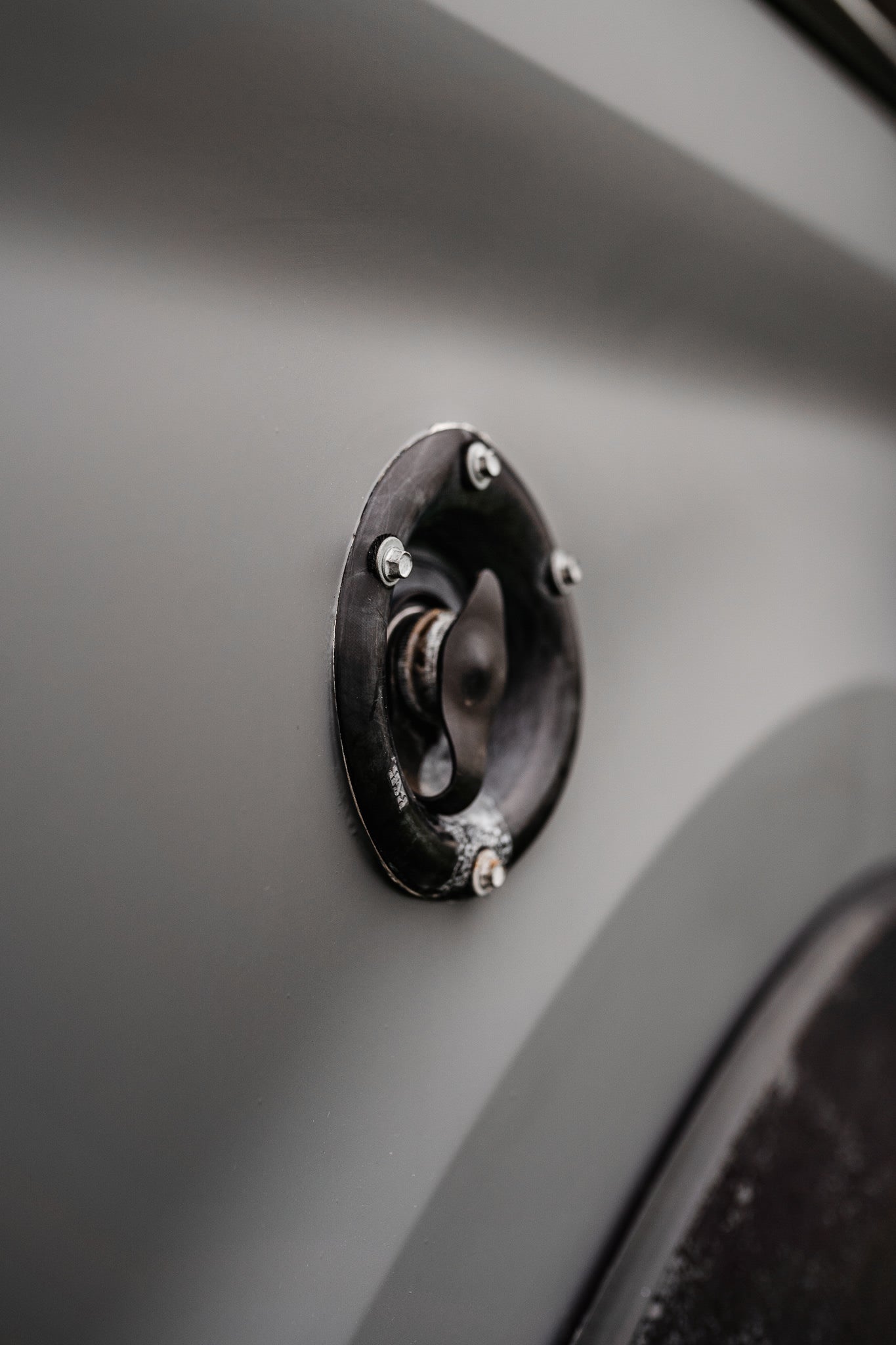 Black access cap on a grey RV rental's side, likely for fuel or water. Functional vehicle detail.