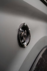 Black access cap on a grey RV rental's side, likely for fuel or water. Functional vehicle detail.