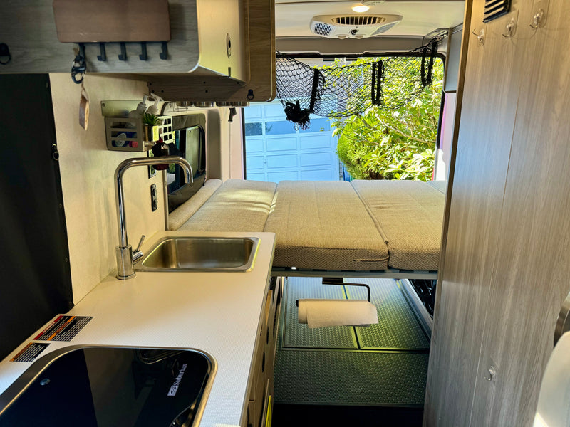 RV rental interior: A bright camper van layout with a compact kitchen (sink, stove) and a convertible bed, ideal for travel. — photo 6