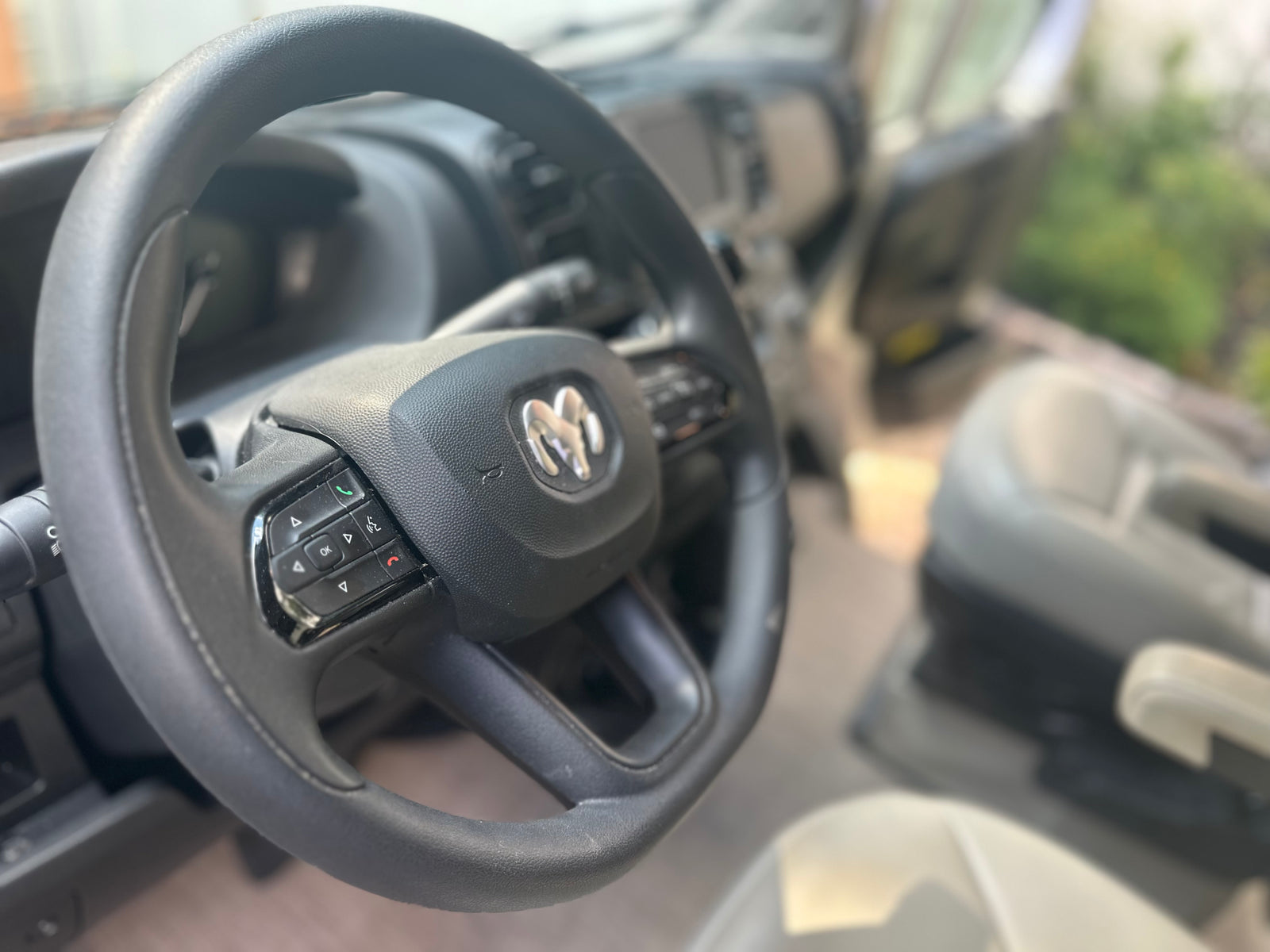 Interior of a Ram van or RV rental, focusing on the steering wheel with its distinctive logo and control buttons.