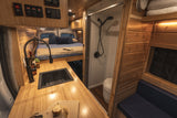 Cozy RV rental interior: wood-paneled van with kitchen sink, bed, and integrated shower/toilet. Your mobile home adventure.