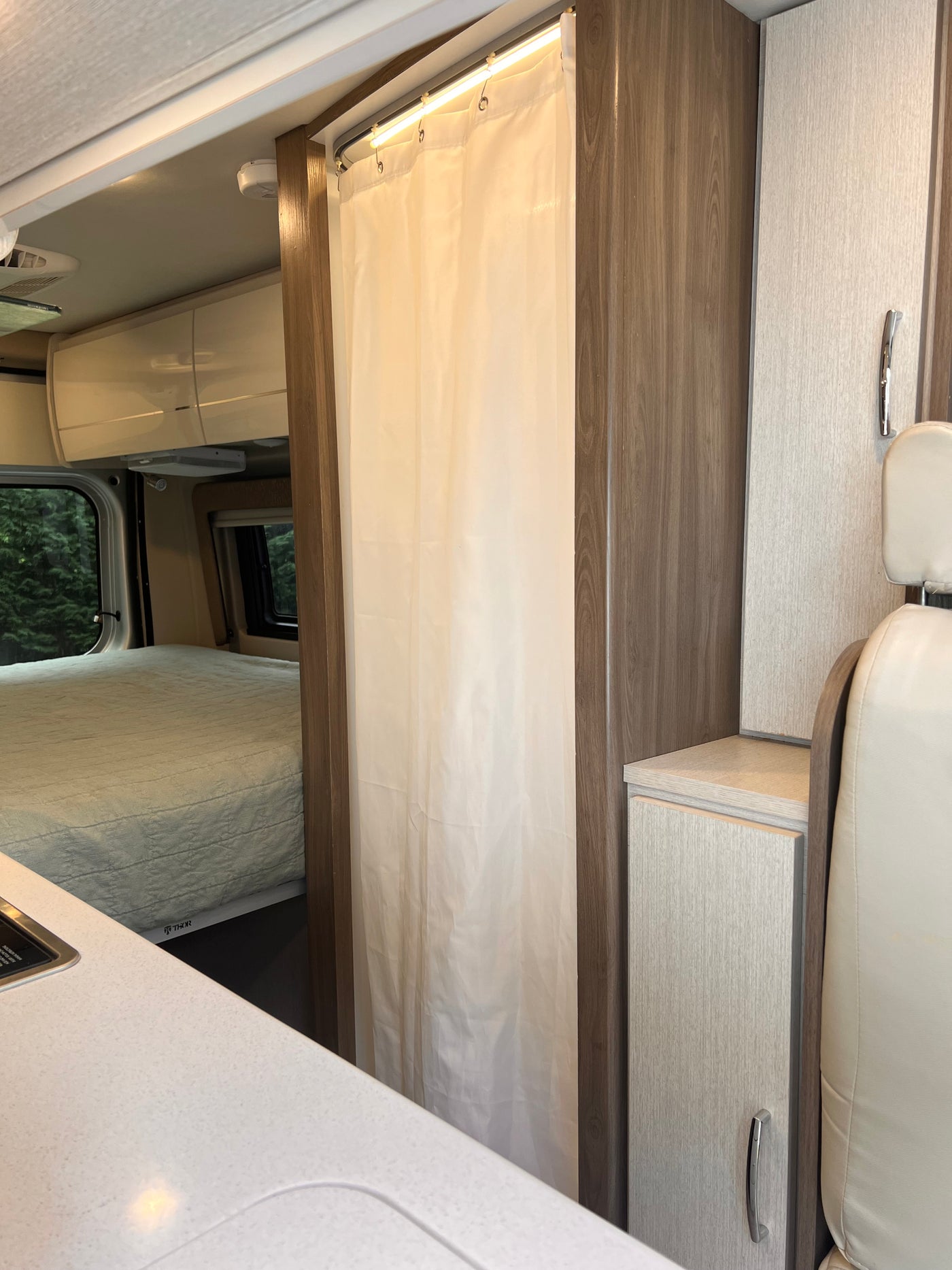 Cozy RV rental interior: a bed, shower curtain, kitchen counter, and storage maximize space for travel adventures. — photo 8