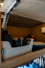 Looking into a well-organized RV rental kitchen cabinet, you see black travel mugs, a pot, and bowls, optimized for small spaces.