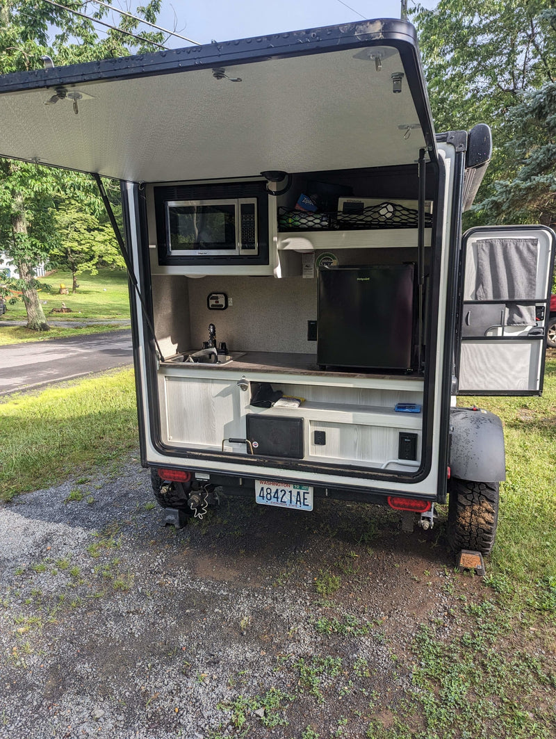 This RV rental features a rear hatch opening to an outdoor kitchen, complete with a microwave, sink, and mini-fridge, ideal for travel. — photo 13
