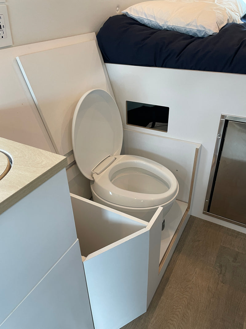 This RV rental features a compact, integrated bathroom with a toilet, adjacent bed, sink area, and mini-fridge in a small space. — photo 15