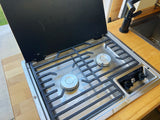 Compact Dometic stove & sink in an RV rental kitchen. Features a two-burner cooktop, black cover, and wood counter.
