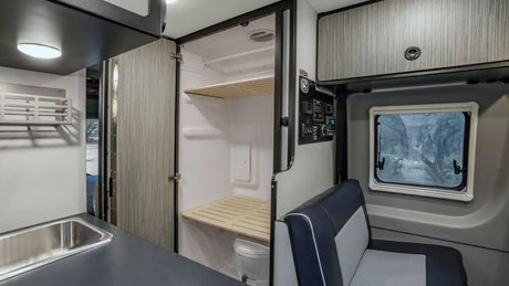 RV rental interior showcasing a compact kitchen, a clever wet bath with toilet and wooden shower shelves, plus seating.