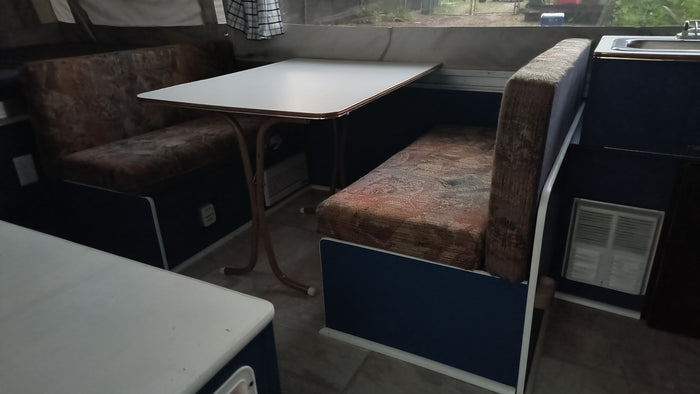 RV rental camper: Cozy dinette with patterned benches & white table. Sink visible, ready for your road trip.