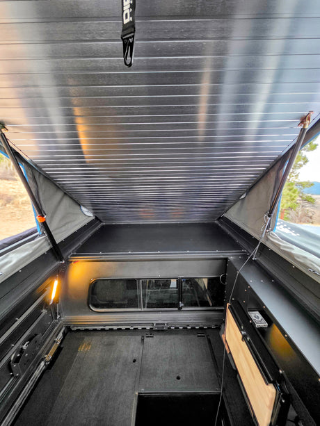 Explore this spacious rv rental's pop-top camper interior, featuring a raised sleeping area, side windows, and convenient storage.