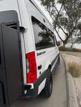 White Sanctuary campervan rv rental, customized with a rear cargo box & off-road tires, ready for outdoor adventure by the water.