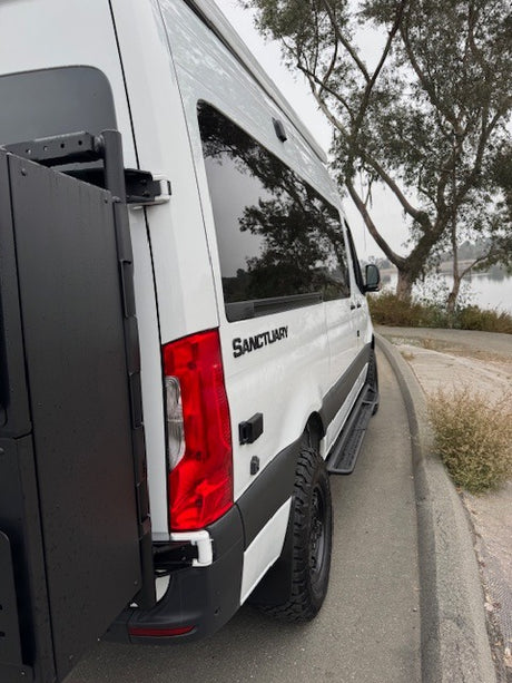 White Sanctuary campervan rv rental, customized with a rear cargo box & off-road tires, ready for outdoor adventure by the water.