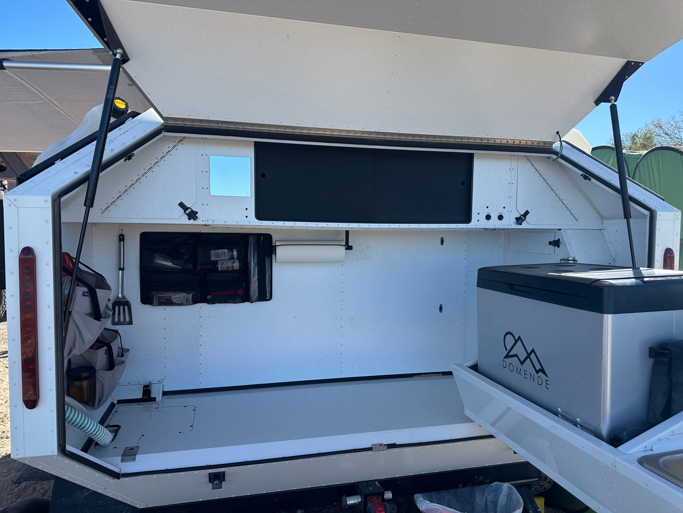 RV rental: Open outdoor kitchen of a camper, revealing a pull-out fridge, organized storage, and utility controls.