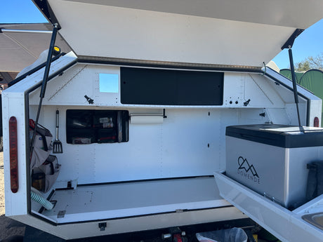RV rental: Open outdoor kitchen of a camper, revealing a pull-out fridge, organized storage, and utility controls.