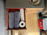 Overhead view of an RV rental's organized kitchen drawer, featuring rolled towels, toilet paper, next to a compact sink.