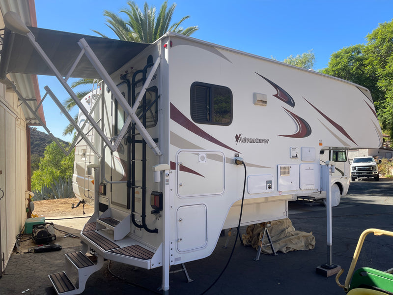 White Adventurer truck camper with extended awning & power connection, parked outdoors with stabilizing jacks. Perfect for rv rental trips. — photo 1
