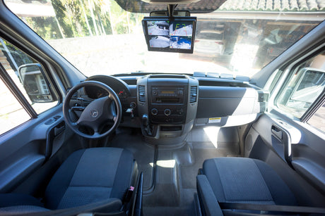 Interior of an RV rental van, highlighting the dashboard, steering wheel, and a monitor displaying multiple camera views for parking.