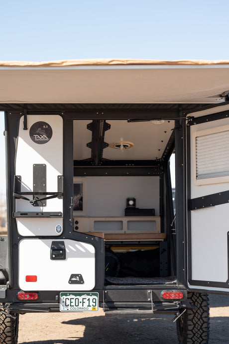 Open rear hatch of a TAXA Outdoors camper, an ideal rv rental for adventure. Shows organized mobile living space.
