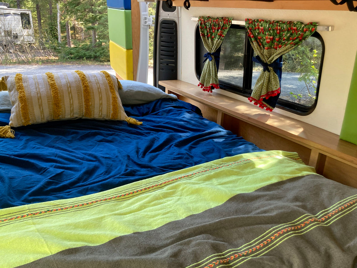 Explore a cozy RV rental: bed, striped blanket, and unique strawberry curtains. Van life comfort in nature. — photo 4