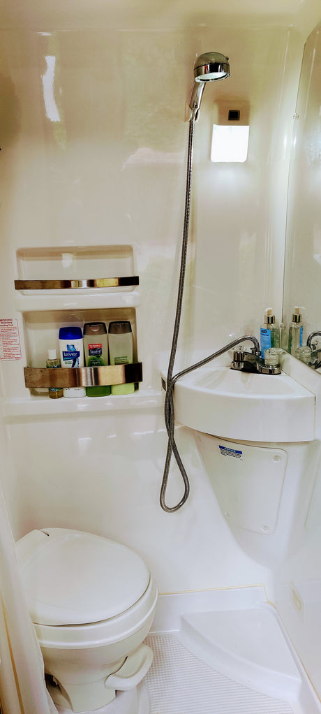 Inside an RV rental: a compact, all-in-one bathroom with toilet, corner sink, and handheld shower. Ideal for road trip comfort.