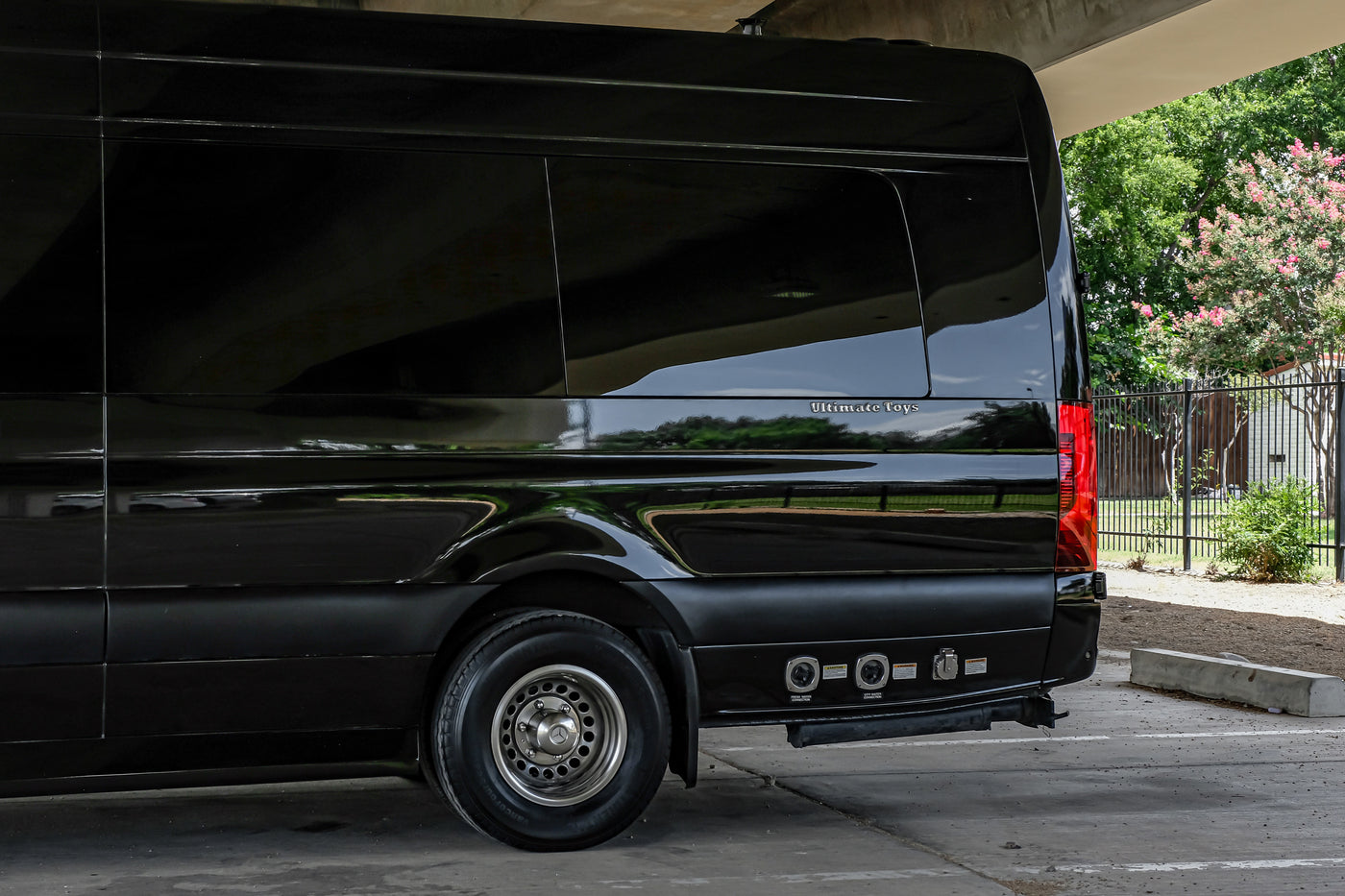 Black luxury RV rental from Ultimate Toys, seen from the rear side. Features fresh and city water connections for convenient use. — photo 13