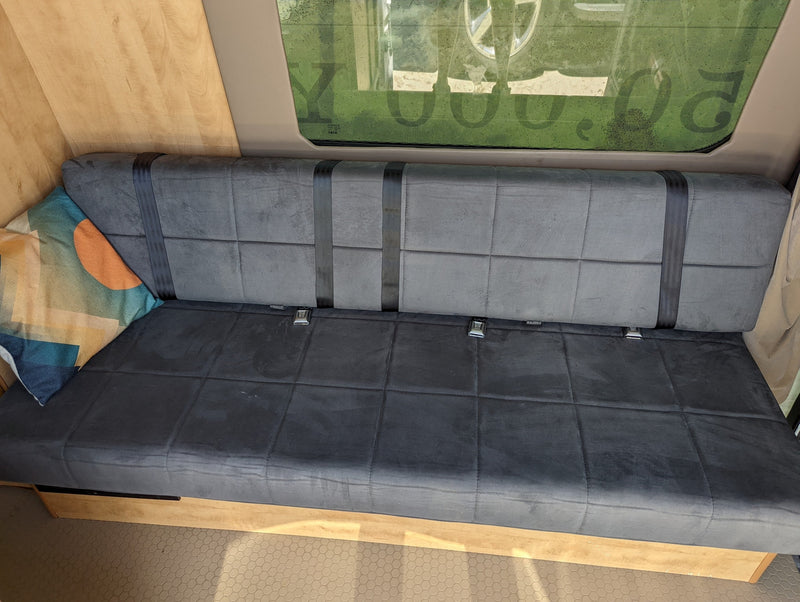 RV rental interior shows a gray bench seat with black seatbelts, a patterned pillow, and wooden walls next to a window. — photo 8