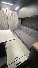Spacious RV rental interior: grey sofa, white table, overhead lights, storage, and modern aesthetic.