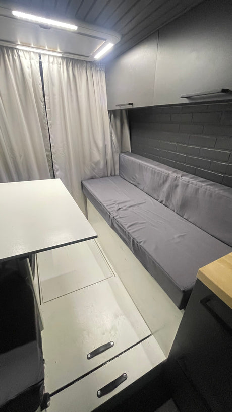 Spacious RV rental interior: grey sofa, white table, overhead lights, storage, and modern aesthetic.