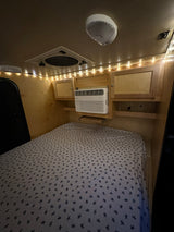 Comfortable RV rental interior featuring a bed with turtle-patterned sheets, AC unit, and ambient string lights.