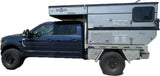 Dark blue Ford truck with off-road tires and a Four Wheel Hawk pop-up truck camper, ideal for an rv rental.